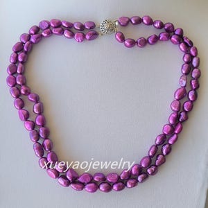 Könnte beinhalten: Eine zweireihige Halskette aus violetten Süßwasserperlen. Die Halskette hat einen silbernen Verschluss.