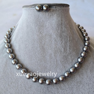 Puede incluir: Un collar de perlas grises y un juego de pendientes a juego exhibidos en un maniquí gris. El collar presenta perlas grandes y redondas. Los pendientes son simples tachuelas. El texto "xueyaojewelry" es visible.