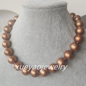 May include: A brown pearl necklace with a large, round pearl in the center. The necklace is on a white mannequin bust.