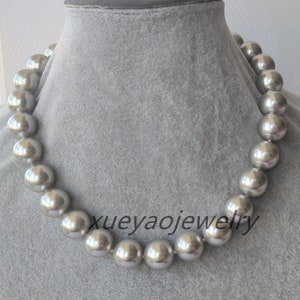 May include: A silver pearl necklace with large, round pearls. The necklace is displayed on a grey fabric background.