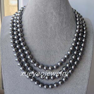 Puede incluir: Un collar de tres hilos con cuentas esféricas de color gris oscuro. Las cuentas son de tamaño uniforme y están ensartadas, creando un efecto de capas. El collar se exhibe sobre un busto de maniquí gris. El texto "xueyaojewelry" es visible.