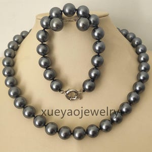Könnte beinhalten: Ein Set bestehend aus einer langen Halskette und einem Armband, beide aus runden, dunkelgrauen, glänzenden Perlen gefertigt. Das Armband hat einen silberfarbenen runden Verschluss. Der Text xueyaojewelry ist in der Bildmitte zu sehen.