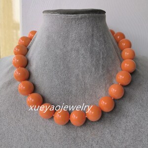 Könnte beinhalten: Klobiges orangefarbenes Perlenhalsband, präsentiert auf einer grauen Schaufensterpuppe. Die Halskette besteht aus großen, runden Perlen, die aufgereiht sind. Der Text "xueyaojewelry" ist sichtbar. Die Perlen haben eine glänzende Oberfläche.