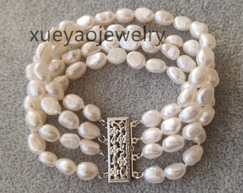Peut inclure: Un bracelet en perles d'eau douce blanches avec un fermoir argenté. Le bracelet est composé de quatre rangs de perles et présente un délicat motif floral sur le fermoir.
