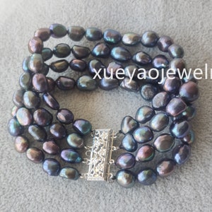 May include: A four-strand bracelet made of dark, iridescent black pearls with a silver clasp. The pearls are oval-shaped and have a slightly irregular shape.