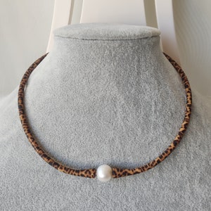 May include: A brown and black leopard print choker necklace with a single white pearl in the center.