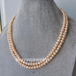 Op de afbeelding: Een dubbele rij parelketting met lichtroze parels. De ketting is om de nek van een mannequin.