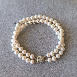 Op de afbeelding: Een dubbele rij parel armband met een zilveren sluiting. De parels zijn wit en rond.