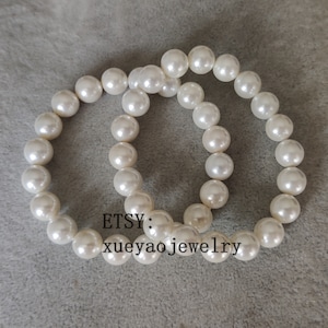 May include: Two white pearl bracelets, one on top of the other, with the text "ETSY: xueyaojewelry" on the bottom.