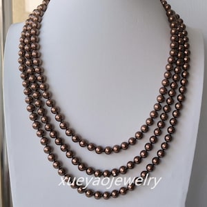Może przedstawiać: Trzyrzędowy naszyjnik z brązowymi, kulistymi koralikami. Naszyjnik jest prezentowany na białym manekinie. Tekst "xueyaojewelry" jest widoczny na dole obrazu.