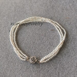 Peut inclure: Un collier de perles blanches avec un fermoir argenté. Le collier est composé de plusieurs rangs de perles.