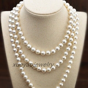 Könnte beinhalten: Eine dreireihige Perlenkette mit weißen Perlen. Die Kette liegt auf einer weißen Mannequin-Büste. Der Text "xueyajojewelry" ist auf der Kette sichtbar.