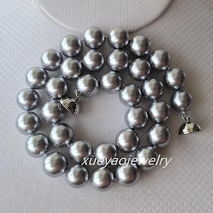 Peut inclure: Un collier de perles argentées avec un fermoir argenté. Les perles sont grandes et rondes.