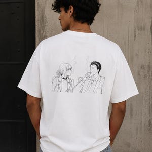 Puede incluir: Una camiseta blanca de manga corta con un gráfico de arte lineal en blanco y negro en la espalda. La ilustración muestra a dos figuras sentadas una frente a la otra, ambas fumando, con finas volutas de humo elevándose sobre sus cabezas.