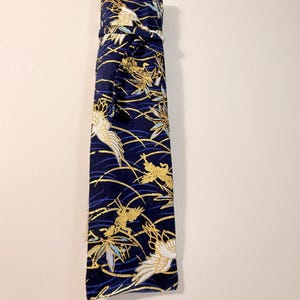 May include: A navy blue fabric item with a repeating pattern of gold and white birds and foliage. The item is tied at the top with a matching fabric tie. The design includes gold, white, and blue accents.