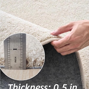 Puede incluir: Primer plano de una alfombra beige con un pelo grueso y texturizado. El grosor de la alfombra es de 1,27 cm. La alfombra tiene un reverso gris oscuro y un borde beige claro. El texto "Thickness: 0.5 in" se muestra en la parte inferior.