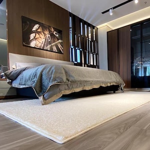 Puede incluir: Un dormitorio moderno con una cama grande, una colcha gris y una alfombra crema. La habitaci&oacute;n tiene paneles de madera oscura y una gran obra de arte enmarcada en la pared. La habitaci&oacute;n est&aacute; bien iluminada.