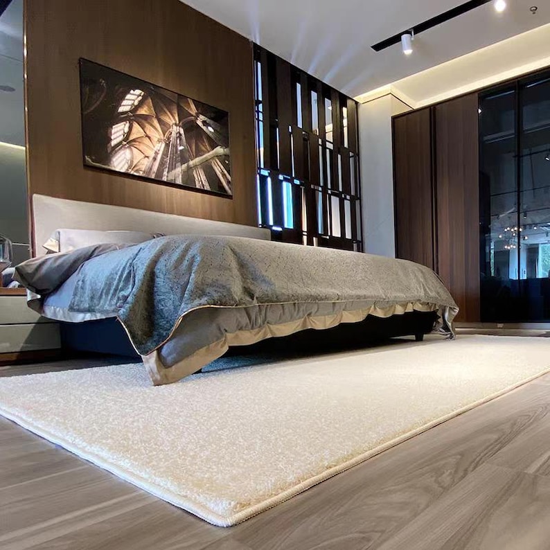 Puede incluir: Un dormitorio moderno con una cama grande, una colcha gris y una alfombra crema. La habitaci&oacute;n tiene paneles de madera oscura y una gran obra de arte enmarcada en la pared. La habitaci&oacute;n est&aacute; bien iluminada.