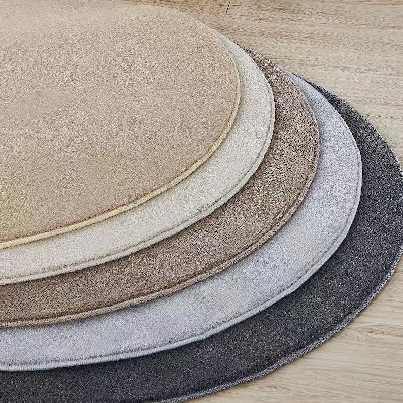 Puede incluir: Una colecci&oacute;n de cinco alfombras redondas en tonos neutros variados, incluyendo beige, crema, marr&oacute;n, gris y antracita. Las alfombras est&aacute;n dispuestas en un patr&oacute;n semicircular en capas, mostrando sus diferentes colores y texturas. Las alfombras est&aacute;n hechas de un material suave y afelpado.