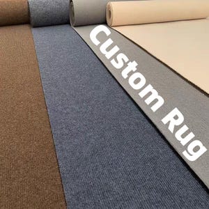 Puede incluir: Una selección de alfombras enrolladas en varios colores, incluyendo marrón, gris y beige. El texto "Custom Rug" se muestra en blanco sobre la alfombra gris, indicando un producto personalizable. Las alfombras tienen una superficie texturizada.