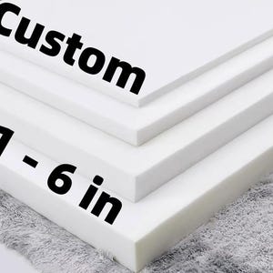 May include: Stack of white foam sheets, labeled "Custom" and "1 - 6 in." The foam is layered, with varying thicknesses. The bottom layer rests on a gray, textured surface.
