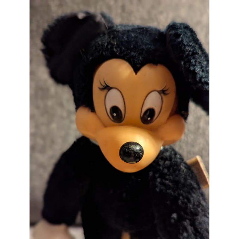 May include: A vintage Minnie Mouse plush doll with a black body and head, and a yellow face. The doll has large, expressive eyes and a black nose. The plush is in good condition, showcasing a classic Disney character.