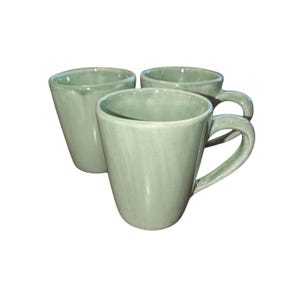 May include: Three pale green ceramic mugs with curved handles. The mugs have a smooth, slightly textured surface and a simple design. Suitable for tea, coffee, or other drinks. Each mug is approximately 10 cm tall.