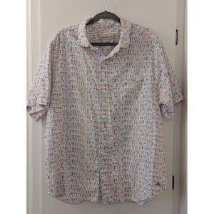 May include: A short-sleeved button-down shirt in white featuring an all-over print of small, colorful cocktail glasses and tropical drink icons in shades of blue, orange, and tan. The shirt has a standard collar and a single chest pocket.