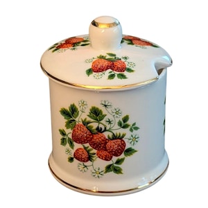 May include: A white ceramic sugar bowl with a matching lid featuring a gold-trimmed rim and knob. The exterior is decorated with a botanical pattern of red strawberries, green leaves, and small white flowers on both the body and lid.