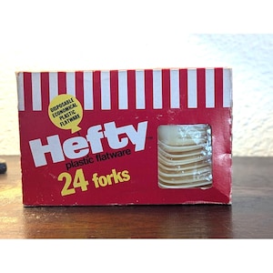 May include: A red and white striped box of Hefty plastic forks. The box has the words "Hefty plastic flatware" and "24 forks" printed on it. A clear plastic window shows the forks inside.