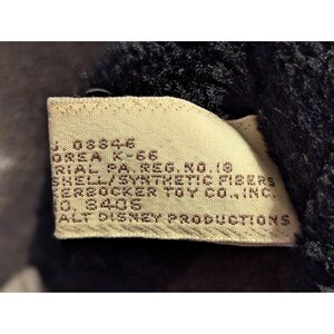 May include: Close-up of a tan tag with brown text. The tag reads "J. 08846 OREA K-66 RIAL PA. REG. NO. 18 SHELL/SYNTHETIC FIBERS KERBOCKER TOY CO., INC. 0. 8405 ALT DISNEY PRODUCTIONS."