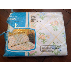 Puede incluir: Una sábana plana de tamaño completo en su embalaje original. La sábana es blanca con un estampado floral en rosa, amarillo y azul. El embalaje dice "Iron Muslin" y "One Flat Sheet - Full Size". El tamaño final es de 206 cm x 251 cm.