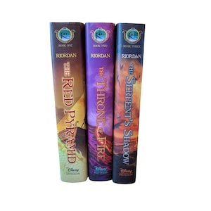 Könnte beinhalten: Drei gebundene Bücher aus der Reihe The Kane Chronicles von Rick Riordan mit den Titeln The Red Pyramid, The Throne of Fire und The Serpent's Shadow. Jeder Buchrücken zeigt das Disney Hyperion Logo, die Bandnummer und farbige Grafiken.