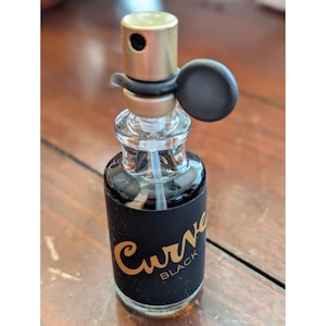 May include: A white ceramic mug with a black handle and the text "But First, Coffee" in a bold, black font. The mug is set against a blurred background, suggesting a cozy setting.