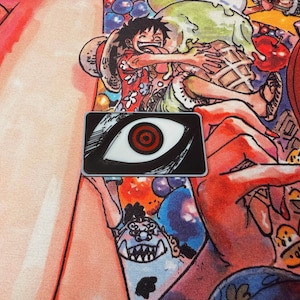 May include: A rectangular pin featuring a stylized eye design with a white iris and a red spiral pupil, set against a black background. The pin is placed on a colorful background with manga-style illustrations.