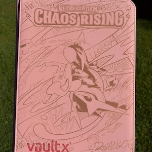 Op de afbeelding: Roze kaartenbinder met de tekst "MEGA EVOLUTION CHAOS RISING" en een karakterillustratie. Het Vault X-logo staat onderaan. De binder wordt tegen een groene achtergrond gehouden.