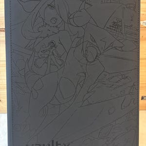 Puede incluir: Un archivador de cartas gris oscuro con una ilustración detallada de personajes de anime. La cubierta presenta un borde cosido y el logotipo "vaultx" en la parte inferior. La obra de arte está grabada en la cubierta.