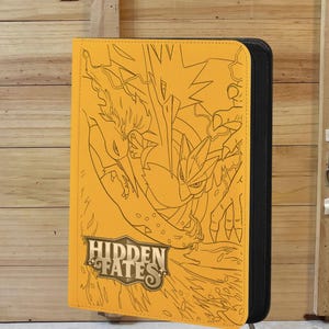 Op de afbeelding: Een gele kaartenbinder met een zwarte rits en de woorden "Hidden Fates" in gouden letters. De voorkant van de binder heeft een zwarte omtrekillustratie van twee mythische wezens.