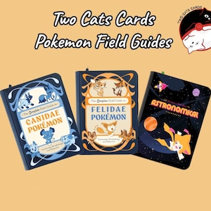 Op de afbeelding: Drie rechthoekige boeken getiteld Two Cats Cards Pokemon Field Guides. Het linkerboek is blauw met de tekst Canidae Pokemon. Het middelste boek is blauw met de tekst Felidae Pokemon. Het rechterboek is zwart met de tekst Astronomical Phenomena.