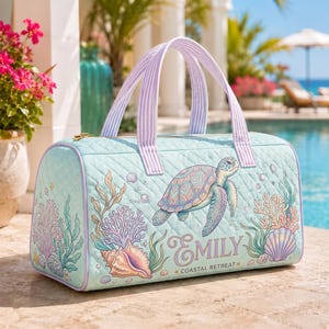 May include: A light mint green quilted duffel bag featuring a sea turtle, coral, and seashell print. The bag has lavender and white striped handles and the text "Emily" and "Coastal Retreat" printed on the front in a decorative script font.