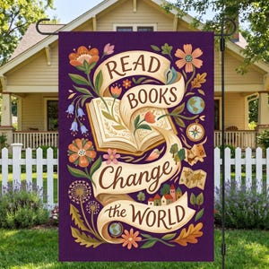 May include: A purple garden flag with the words "Read Books Change the World" in a decorative font. The flag features an open book, flowers, a globe, and a compass. The design is set against a backdrop of a house and a white picket fence.