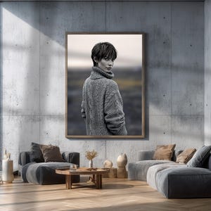 May include: A framed black and white photograph of a person wearing a gray cable-knit turtleneck sweater. The photograph is displayed in a modern living room with gray furniture and a wooden coffee table.