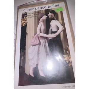May include: A package featuring a pattern for Elinor Peace Bailey's "Shady Lady and Dapper Dan" dolls. The dolls are depicted in a romantic pose, with the woman in a floral dress and the man in a tuxedo. The package has a green price tag.