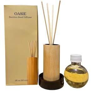 May include: OASIE Bamboo Reed Diffuser set including a tall gold box with text, a cylindrical bamboo holder on a black base with four reeds, and a round glass bottle filled with 3 fl oz of yellow liquid fragrance oil for home scenting.
