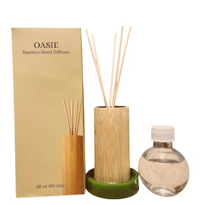 Puede incluir: Set de difusor de varillas de bambú OASIE que incluye una caja beige con texto, un soporte cilíndrico de bambú con cuatro varillas, una base circular verde y una botella de vidrio transparente con tapa blanca, con 90 ml de capacidad.