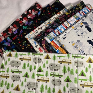 Puede incluir: Un juego de seis manteles individuales de tela con diferentes patrones. Los manteles individuales son negros con notas musicales de colores, vichy rojo y blanco con mariposas, un patrón azul y blanco con notas musicales, un patrón blanco y negro con notas musicales y texto, un patrón gris y azul con texto e imágenes de un oso y una tienda de campaña, y un patrón blanco con árboles verdes, tiendas de campaña y autocaravanas.