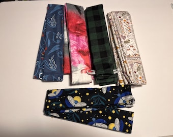 May include: An assortment of fabric headbands in various patterns. Designs include a navy blue floral print, a pink tie-dye, a green and black plaid, a cream-colored mountain scene, and a black headband with blue and yellow firefly illustrations.