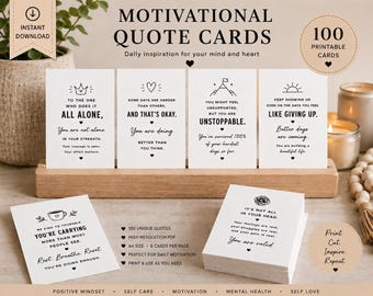 May include: A set of 100 white motivational quote cards with black text and minimalist line art icons. Four cards are displayed upright in a wooden stand, while two additional cards rest on the surface. The cards feature phrases like You are not alone and You are valid.