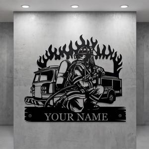 May include: Black metal wall art featuring a firefighter kneeling in front of a fire truck, with flames rising behind them. The text "YOUR NAME" is displayed below. A decorative piece for fire departments or first responders.