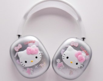 以下が含まれることがあります： 白いヘッドバンドが付いたシルバーのヘッドフォン。各イヤーカップには、ピンクのリボンと「Hello Kitty」の文字が入ったハローキティのデザインが施されています。デザインには、ピンクのリボン、星、小さなキャラクターイラストが含まれています。